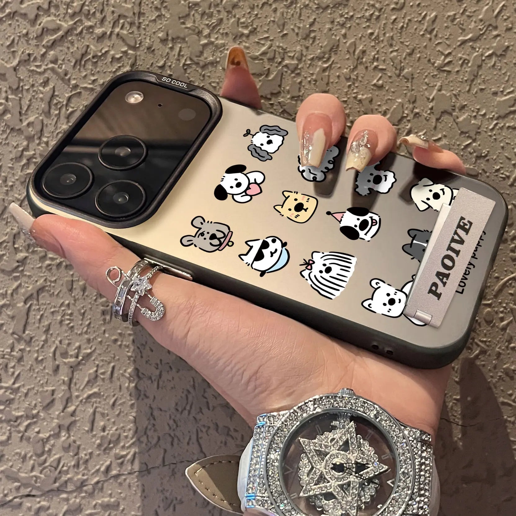 Phone case with cartoon designs held by a hand against a textured wall.